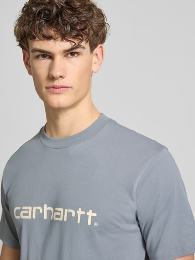 Männermodel trägt T-Shirt aus Baumwolle Modell 'Script' von Carhartt Work In Progress in Grau mit Label-Print, Nahaufnahme Oberkörper.