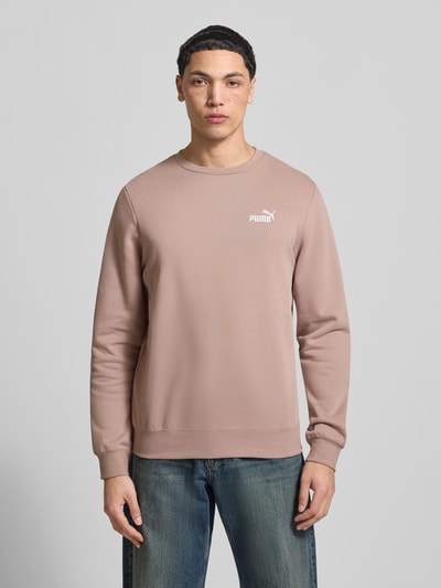 Męski model nosi Regular Fit Sweatshirt mit Logo-Stitching od PUMA PERFORMANCE, mieszanka bawełny, okrągły dekolt, elastyczne wykończenia, kolor jasnobrązowy, widok całej sylwetki z przodu.