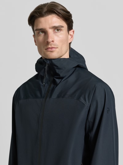 Mannelijk model draagt Regular Fit Jacke mit Logo-Print Modell 'Treeline' van PEAK PERFORMANCE in donkerblauw met capuchon en steekzakken, Nahaufnahme Oberkörper.
