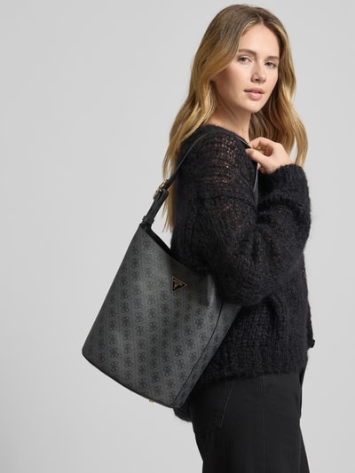 Frauenmodel trägt Handtasche mit Logo-Muster Modell 'MERIDIAN II' von Guess, grau-schwarz, Label-Applikation, Nahaufnahme Oberkörper. Breite 28 cm, Länge 28 cm, Tiefe 16 cm, Schulterriemen 64 cm, Magnetverschluss, weiche Textur.