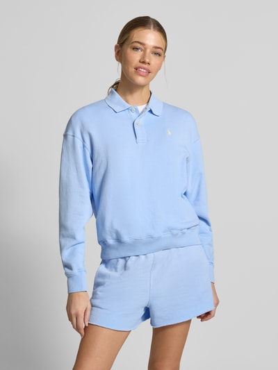Modelka kobieca nosi Regular Fit Sweatshirt aus Baumwoll-Mix od Polo Ralph Lauren w jasnoniebieskim kolorze, bawełniana gładka tekstura, haftowane logo, krój regular fit, długi rękaw, polokołnierzyk, 2-guzikowe zapięcie, wykończenia ściągaczowe, widok na cały korpus z przodu.