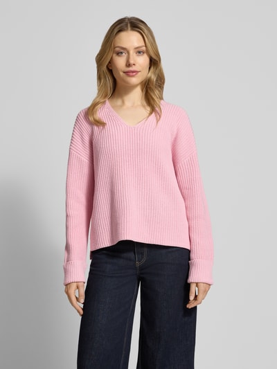 Kobiece modelka nosi Oversized Strickpullover aus Baumwoll-Mix od s.Oliver RED LABEL w kolorze różowym, faktura prążkowanego bawełnianego miksa, dekolt w serek, rękawy 3/4 z mankietem, luźny krój, widoczne przeszycia label, jednolity kolor, rozcięcia po bokach, widok całej sylwetki z przodu.