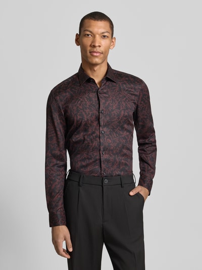 Männermodel trägt Slim Fit Businesshemd aus Lyocell Modell 'KENNO' von HUGO mit Allover-Muster in Rot-Schwarz, Ganzkörperansicht von vorne.