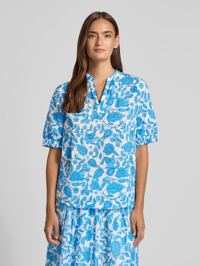 Frauenmodel trägt Bluse mit elastischen Ärmelabschlüssen von More & More, blaue Blumen auf weiß, Reine Baumwolle, Regular-Fit, Serafino-Kragen, Ganzkörperansicht von vorne.