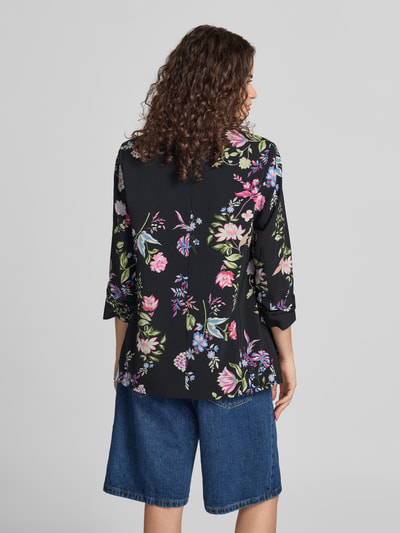 Kobieta nosi Shaped Fit Longblazer mit Schalkragen model 'BOSELLA' od PIECES, kwiatowy wzór, ciemne kolory, widok całej sylwetki z tyłu.