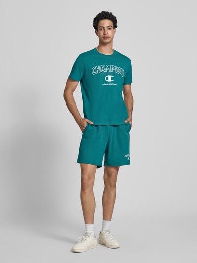 Männermodel trägt T-Shirt mit Label-Print und Rundhalsausschnitt von CHAMPION in Türkis, Reine Baumwolle, Regular-Fit, Ganzkörperansicht von vorne. Rückenlänge bei Größe M: 68 cm.
