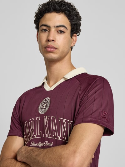 Männermodel trägt Regular Fit T-Shirt mit Logo-Stitching Modell 'Heritage' von KARL KANI in Dunkelrot mit Umlegekragen, Nahaufnahme Oberkörper. Herren T-Shirt mit Rückenlänge 70 cm in Größe M.