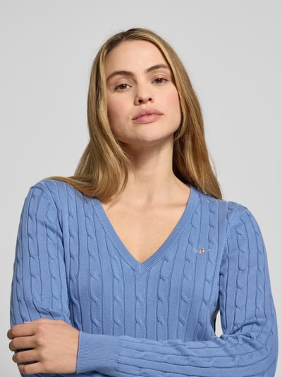 Kobiece modelka nosi niebieski Strickpullover mit Zopfmuster und Label-Stitching od Gant, wąski krój, dekolt V, zbliżenie na górę ciała.