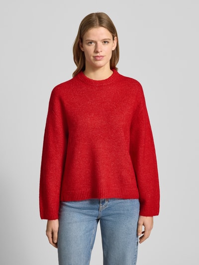 Vrouwenmodel draagt Strickpullover met wol-aandeel van Gina Tricot in rood, los model, geribde boorden, ronde hals, frontale lichaamsopname.