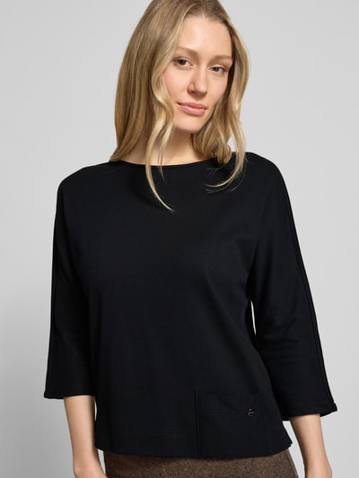 Frauenmodel trägt Shirt mit U-Boot-Ausschnitt und Label-Detail von Marc Cain, schwarz, straight Fit, Baumwoll-Mix, Nahaufnahme Oberkörper.