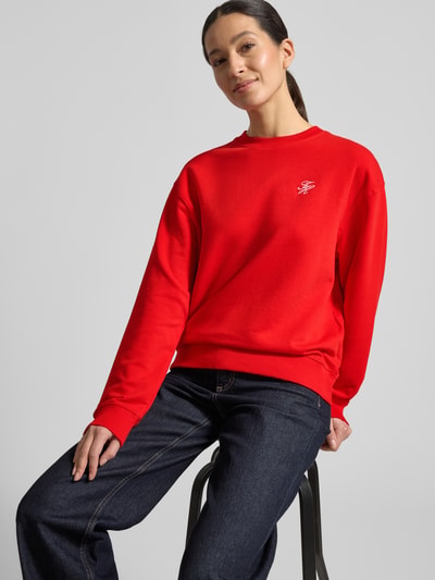 Frauenmodel trägt Regular Fit Sweatshirt aus Baumwoll-Mix von Tommy Hilfiger in kräftigem Rot mit Logo-Detail, Rundhals, lange Ärmel, Sweat-Textur, unifarben, Ganzkörperansicht von vorne.