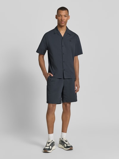 Männermodel trägt Loose Fit Shorts aus Baumwoll-Mix von Lacoste mit feinem Allover-Streifenmuster, Seersucker-Textur, Ganzkörperansicht von vorne.