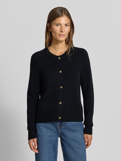 Frauenmodel trägt Strickjacke aus reinem Kaschmir von MYON, schwarze Farbe, gerade Passform, Knopfleiste, Rundhalsausschnitt, Jeans, Ganzkörperansicht von vorne.