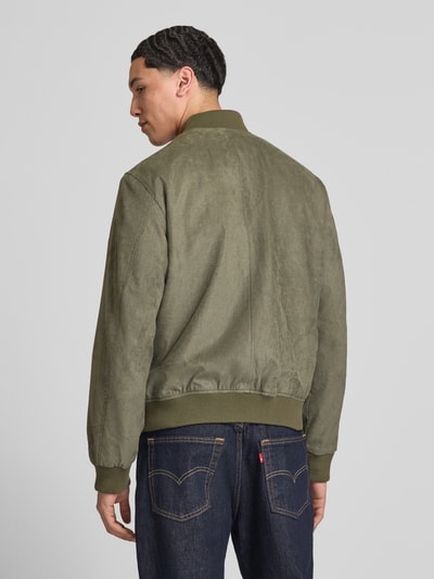Męski model nosi Bomberjacke in Leder-Optik mit Stehkragen von Jack & Jones, kolor oliwkowy, krój regular fit, imitacja skóry, zamek błyskawiczny, wpuszczane kieszenie, długość tyłu w rozmiarze M: 64 cm, szerokość ramion w rozmiarze M: 45 cm, szerokość klatki piersiowej w rozmiarze M: 52 cm, długość rękawów w rozmiarze M: 67 cm, widok całej sylwetki z tyłu.