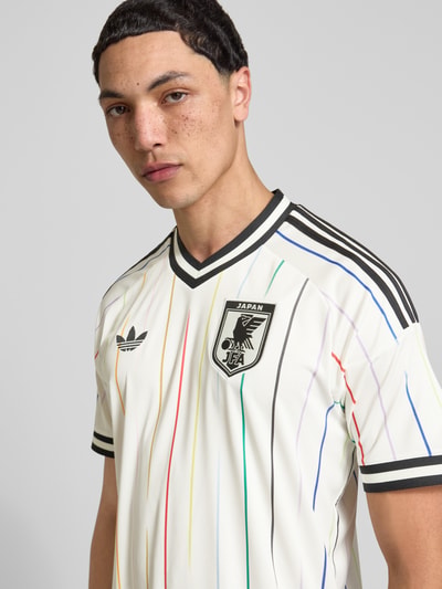 Männermodel trägt Japan Auswärtstrikot 2026 von adidas Sportswear, Mehrfarbig, Regular-Fit, Logo-Applikation, Kontraststreifen, V-Ausschnitt, Kurzarm, CLIMACOOL Technologie, Ganzkörperansicht von vorne.