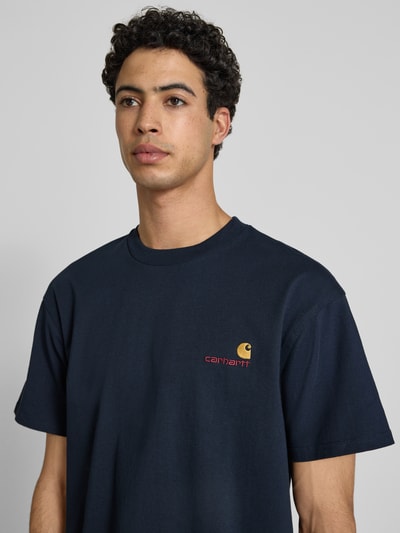 Männermodel trägt T-Shirt mit Label-Stitching und Rundhalsausschnitt von Carhartt Work In Progress in Dunkelblau, Reine Baumwolle, Regular-Fit, Rückenlänge bei Größe M 73 cm, Nahaufnahme Oberkörper.