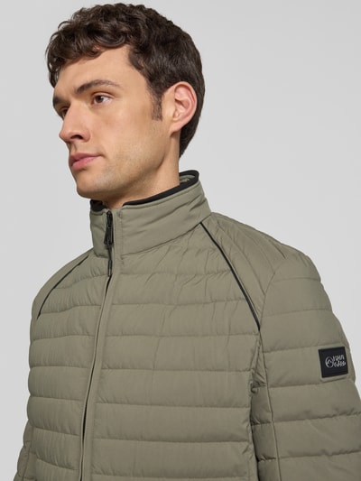 Männermodel trägt Steppjacke mit Stehkragen und Reißverschlusstaschen von NAUTGÅRD in Khaki, Regular Fit, Nahaufnahme Oberkörper. Rückenlänge bei Größe M: 69 cm, Schulterbreite: 40 cm, Brustweite: 46 cm, Ärmellänge: 62 cm.
