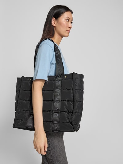 Frauenmodel trägt schwarzen Shopper mit Label-Details von Hey Marly, wattierte Textur, Lange Tragegriffe, Ganzkörperansicht von der Seite. Kontext: Damen Shopper von Hey Marly, offenes Hauptfach, Länge 36 cm, Breite 49 cm, Tiefe 16 cm, Modell 'Best Buddy', Label-Details, Reißverschlussfach innen, Länge Schulterriemen 61 cm.