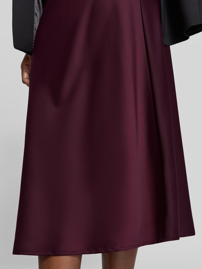Frauenmodel trägt Midirock mit elastischem Bund Modell 'PELLA' von YAS in bordeauxrotem Satin, A-Linie, Nahaufnahme Unterkörper.