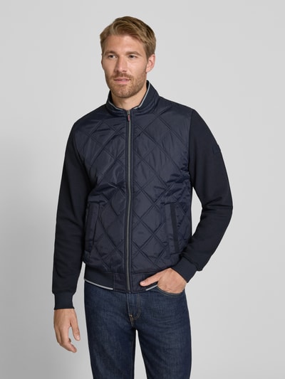Männermodel trägt Regular Fit Collegejacke aus Baumwoll-Mix von Christian Berg Men in Dunkelblau mit Stehkragen und Stepp-Optik, Ganzkörperansicht von vorne.