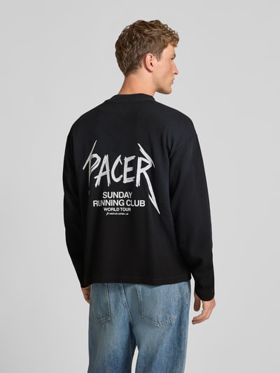 Männermodel trägt schwarzes Regular Fit Sweatshirt aus Baumwoll-Mix Modell 'SRC® Pacer' von ANOTHER COTTON LAB mit Statement-Print, Strukturmuster, Rückenlänge 66 cm, Ganzkörperansicht Rückansicht.