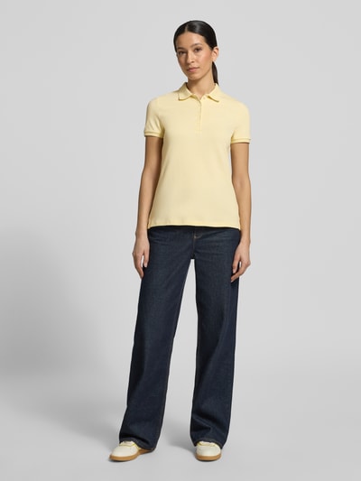 Frauenmodel trägt Slim Fit Poloshirt mit Knopfleiste von Christian Berg Woman, Baumwoll-Elasthan-Mix, Gelb, Seitenschlitze, Ganzkörperansicht von vorne.