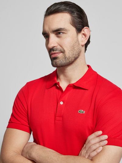 Männermodel trägt Regular Fit Poloshirt aus reiner Baumwolle von Lacoste, unifarbenes Rot, Logo-Detail, Nahaufnahme Oberkörper.