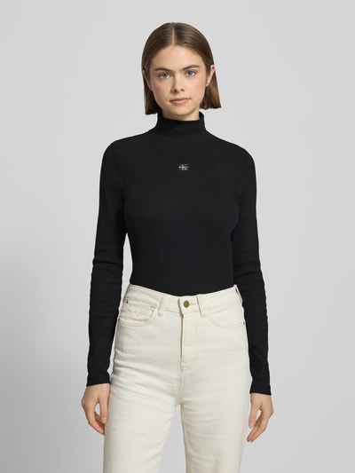 Vrouwenmodel draagt Turtleneck-Pullover met Label-Detail van Calvin Klein Jeans, zwart, mix van katoen en elastaan, nauwsluitend model, opstaande kraag, labeldetail op de borst, ruglengte maat S 56 cm, geheel van voren.