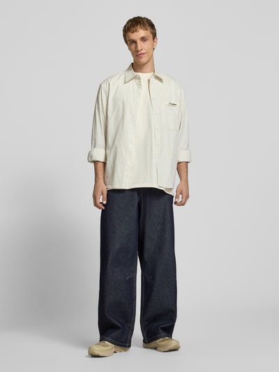 Männermodel trägt Wide Fit Jeans mit Logo-Stitching von KARL KANI, dunkles Denim, 5-Pocket-Design, reine Baumwolle, Ganzkörperansicht von vorne.