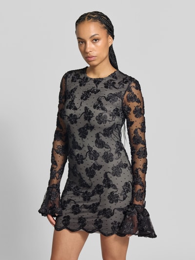 Frauenmodel trägt Minikleid mit floralem Besatz von ROTATE in Schwarz, langärmelig, spitzenverziert, Slim Fit, transparent mit blickdichtem Unterkleid, Ganzkörperansicht von vorne, Kontext: Damen Minikleid, Spitzenstoff, florale Details, Gesamtlänge 88 cm, Brustweite 40 cm, Ärmellänge 84 cm.