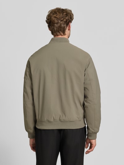 Mężczyznamodel nosi bomberkę z zamkiem błyskawicznym i wpuszczanymi kieszeniami 'Bomberjacke mit Reißverschluss und Eingrifftaschen' od JACK & JONES premium, krój regular fit, stójka, długość tyłu w rozmiarze M: 66 cm, szerokość ramion w rozmiarze M: 42 cm, szerokość klatki piersiowej w rozmiarze M: 60 cm, długość rękawów w rozmiarze M: 68 cm, kolor oliwkowy, tekstura gładka, widok całej sylwetki z tyłu.