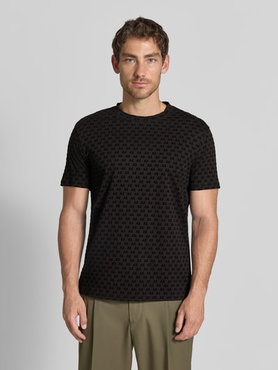 Męski model nosi Regular Fit T-Shirt mit Allover-Print von Armani Exchange, czarny z nadrukiem na całej powierzchni, okrągły dekolt, krój regular fit, z krótkim rękawem, długość tyłu w rozmiarze M: 63 cm, Ganzkörperansicht von vorne.