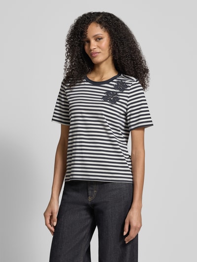 Modelka nosi T-shirt aus Baumwoll-Mix von Christian Berg Woman Selection w czarne i białe paski, ozdobiony kamieniami stras, mieszanka bawełny i elastanu, prosty krój, półrękaw, okrągły dekolt, długość tyłu w rozmiarze 36: 54 cm, ujęcie całej sylwetki z przodu.