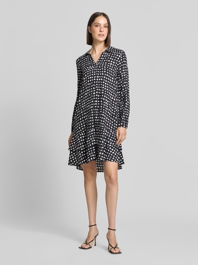 Frauenmodel trägt Knielanges Kleid aus reiner Viskose von Emily Van den Bergh, schwarz mit weißen Punkten, lockerer Schnitt, Umlegekragen, langärmelig, Damen Kleid knielang, Relaxed Fit, Ganzkörperansicht von vorne.