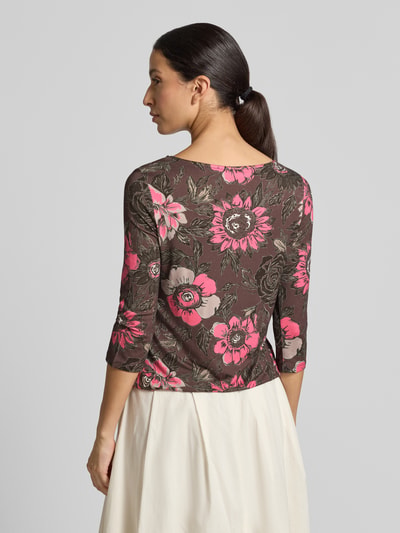 Modelka nosi T-Shirt im Allover-Look mit 3/4-Arm von Christian Berg Woman, mieszanka wiskozy i elastanu, krój slim fit, wzór na całej powierzchni, okrągły dekolt, rękaw o dł. 3/4, Długość tyłu w rozmiarze S: 55 cm, wielokolorowe kwiaty na brązowym tle; całkowite ujęcie z tyłu.