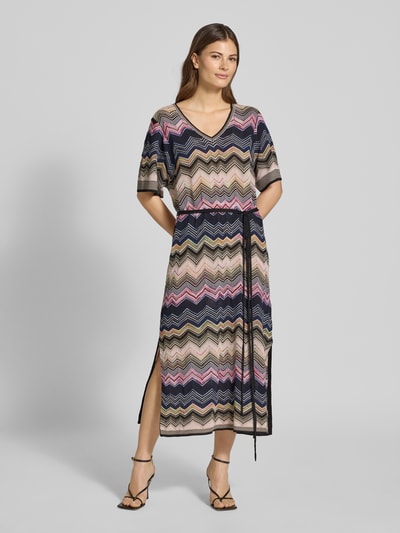 Frauenmodel trägt Strickkleid aus Viskose-Mix mit Bindegürtel von Oui, buntes Zickzack-Muster, gerader Schnitt, V-Ausschnitt, Midikleid, 1/2-Arm, Ganzkörperansicht von vorne.