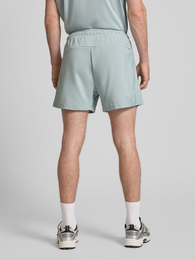 Männermodel trägt Regular Fit Shorts mit Logo-Print von adidas Training in Hellblau, elastischer Bund, Reißverschlusstaschen, Ganzkörperansicht Rückansicht.