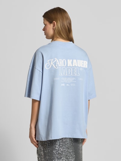 Frauenmodel trägt Oversized T-Shirt mit rückseitigem Statement-Print von Karo Kauer in Hellblau aus Reine Baumwolle mit Rundhalsausschnitt, Oversized-Fit und Label-Print, Rückenlänge bei Größe S: 71 cm, Ganzkörperansicht Rückansicht.