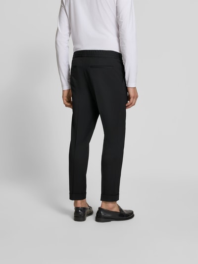 Männermodel trägt Slim Fit Anzughose mit Woll-Anteil von Filippa K, Elastischer-Material-Mix, Eingrifftaschen, Bundfalten, Bund, schwarze Farbe, Ganzkörperansicht Rückansicht.
