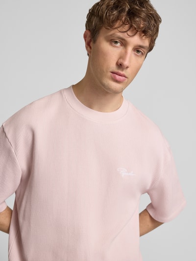 Männermodel trägt Oversized T-Shirt mit Strukturmuster von Pegador in zartem Rosa, Baumwoll-Mix, Rundhalsausschnitt, Logo-Stitching, Nahaufnahme Oberkörper. Rückenlänge bei Größe M: 71 cm, Oversized-Fit, Herren T-Shirt.