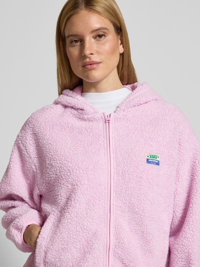 Frauenmodel trägt Jacke aus Teddyfell Modell 'HOKTOWN' von American Vintage in Rosa mit Kapuze, Reißverschluss, Label-Detail, Eingrifftaschen, Regular Fit, Nahaufnahme Oberkörper. Rückenlänge 48 cm, Schulterbreite 57 cm, Brustweite 58 cm, Ärmellänge 49 cm bei Größe XS/S.