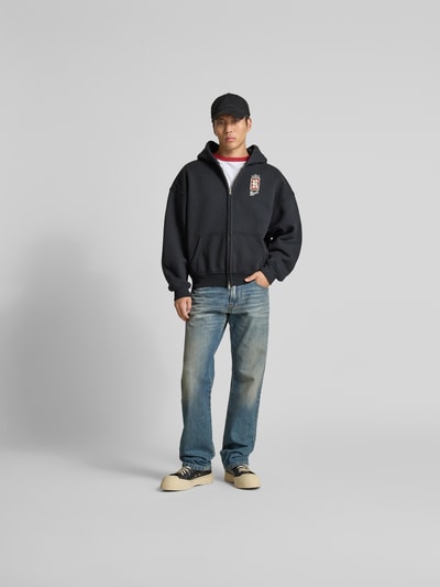 Männermodel trägt Oversized Sweatjacke aus Baumwolle von RHUDE, dunkelblau, Zweiwege-Reißverschluss, Känguru-Tasche, Ganzkörperansicht von vorne