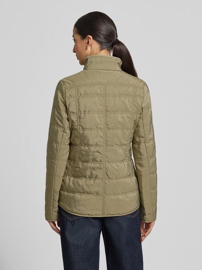 Frauenmodel trägt Steppjacke mit Stehkragen und Reißverschlusstaschen von Fuchs Schmitt, taliowany fason, kolor oliwkowy, faktura matowa, długość tyłu w rozmiarze 36: 65 cm, szerokość ramion w rozmiarze 36: 45 cm, szerokość klatki piersiowej w rozmiarze 36: 42 cm, długość rękawów w rozmiarze 36: 65 cm, ganzkörperansicht rückansicht.