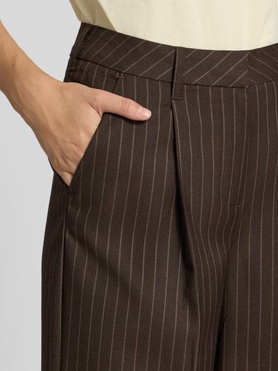 Kobieta nosi spodnie z zakładkami w pasie, krój wide fit od JJXX Wide Fit Hose mit Viskose-Anteil Modell 'Aya Ellis', elastyczna mieszanka materiałów z dodatkiem wiskozy, kanty, zapięcie na haftkę i zamek błyskawiczny, szerokość w rozmiarze S/32: 37 cm, długość wewnętrzna nogawki w rozmiarze S/32: 77 cm, brązowe w jasne paski, zbliżenie na kieszeń, detal.