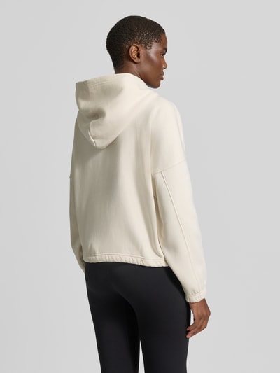 Frauenmodel trägt Sweatjacke mit Logo-Schriftzug von AIMN in Creme, Regular Fit, cropped, Kapuze, langarm, Kängurutasche, Rückansicht.