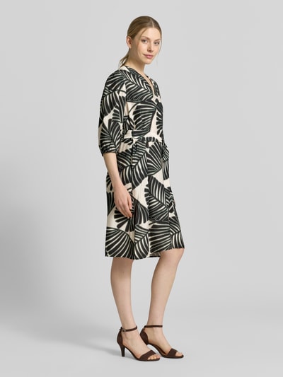 Frauenmodel trägt Knielanges Kleid aus Viskose-Mix mit Tunika-Ausschnitt von Christian Berg Woman Selection, floraler Allover-Print, Tailliert, Halbarm, creme-schwarz, Knielänge, Ganzkörperansicht von vorne.