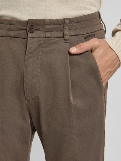 Mężczyzna nosi Regular Fit Hose mit Bundfalten Modell 'CHASY' od Drykorn, brązowy kolor, lyocell-bawełniany mix ze stretchem, zbliżenie na talię.