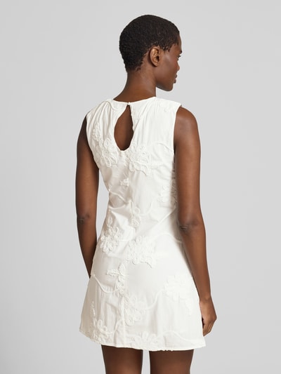 Frauenmodel trägt Minikleid mit floralem Zierbesatz von ROTATE aus reiner Baumwolle in Creme, leicht tailliert, Ganzkörperansicht Rückansicht.