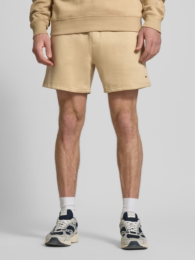Mannelijk model draagt Regular Fit Shorts uit katoenmix van Tommy Jeans, look: effen, logodetail, elastische boord met tunnelkoord, steekzakken, sweat materiaal, kleur beige, voorkant volledig zichtbaar, detailopname onderlichaam