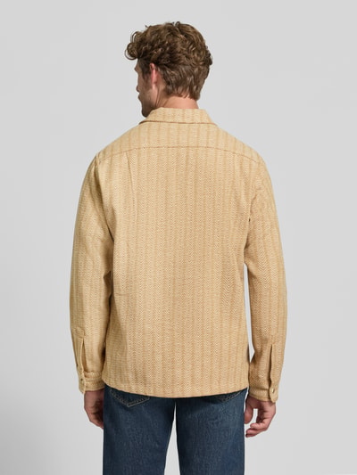Männermodel trägt Relaxed Fit Hemdjacke mit Brusttaschen von Scotch & Soda in Beige mit Allover-Muster und Kentkragen, Ganzkörperansicht Rückansicht. Rückenlänge bei Größe M 75 cm, Knopfleiste und Label-Detail, strukturierte Textur.